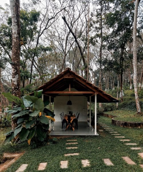 A tranquil outdoor scene featuring two wooden tables placed side-by-side in a lush green garden